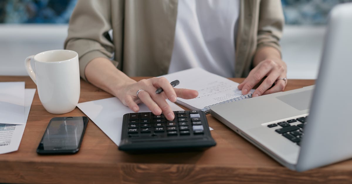 Person using a calculator with laptop and notepad for financial planning